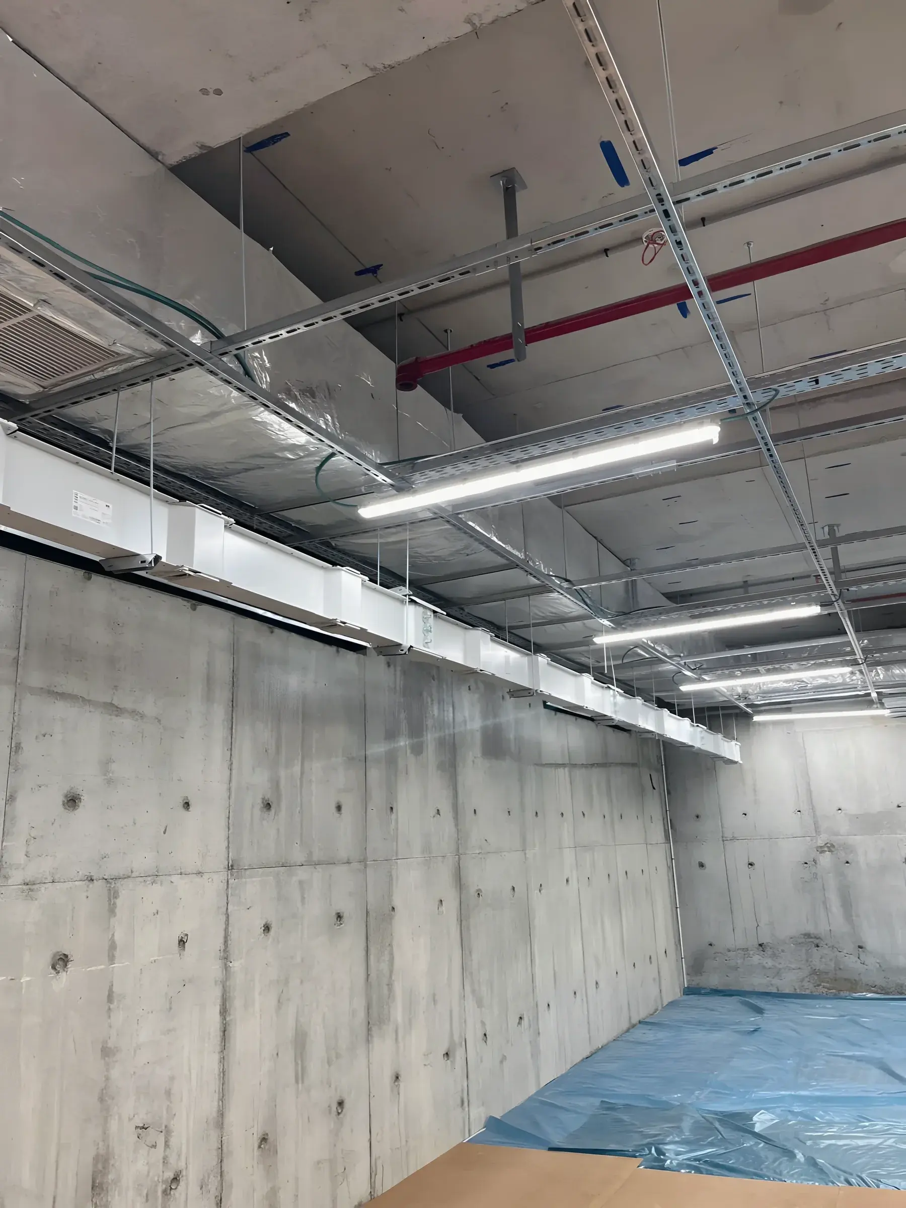 Overhead services in a plant corridor: cable containment, pipework and lighting under a concrete soffit