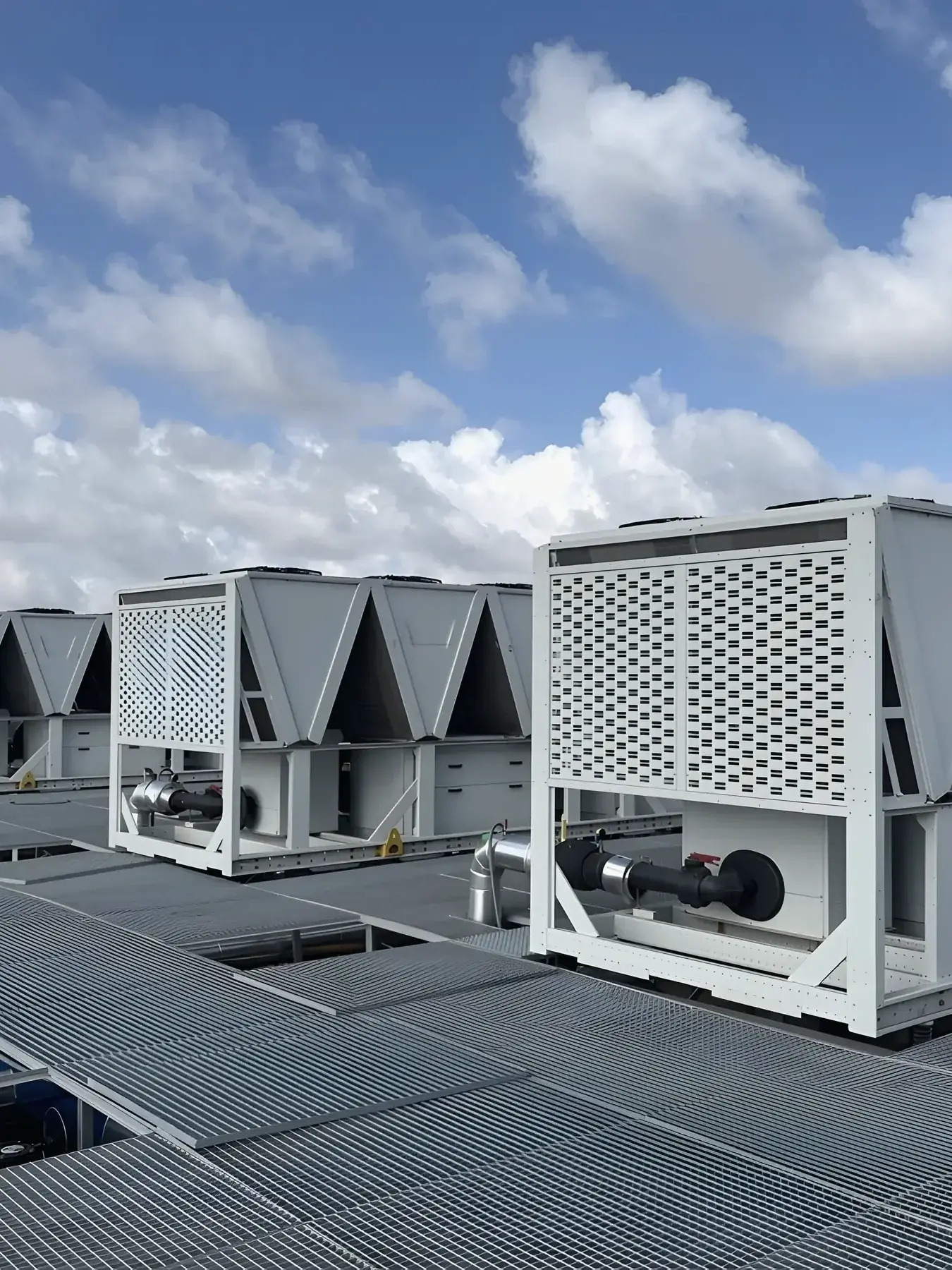 Air-cooled chillers on a rooftop plant deck under a clear sky, seen from the grating walkway