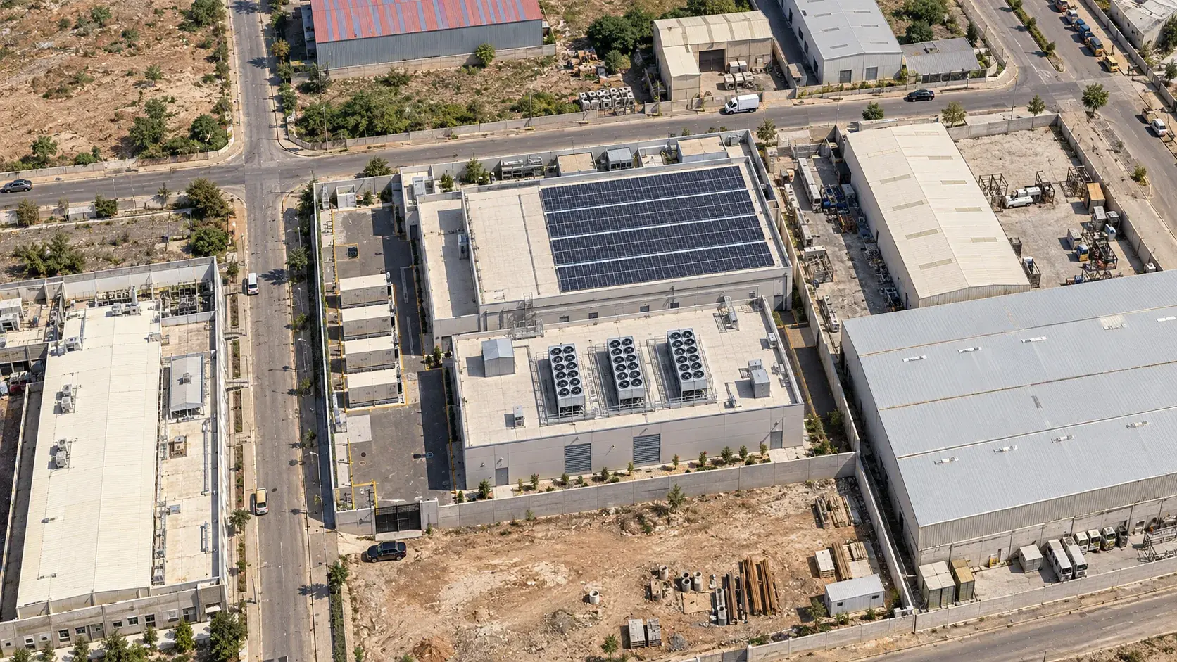 Aerial visualisation of the N+ONE STT data center at Settat Park: the hall with its rooftop photovoltaic array and three roof chillers, the generator row along the yard, the perimeter wall and the industrial park around it