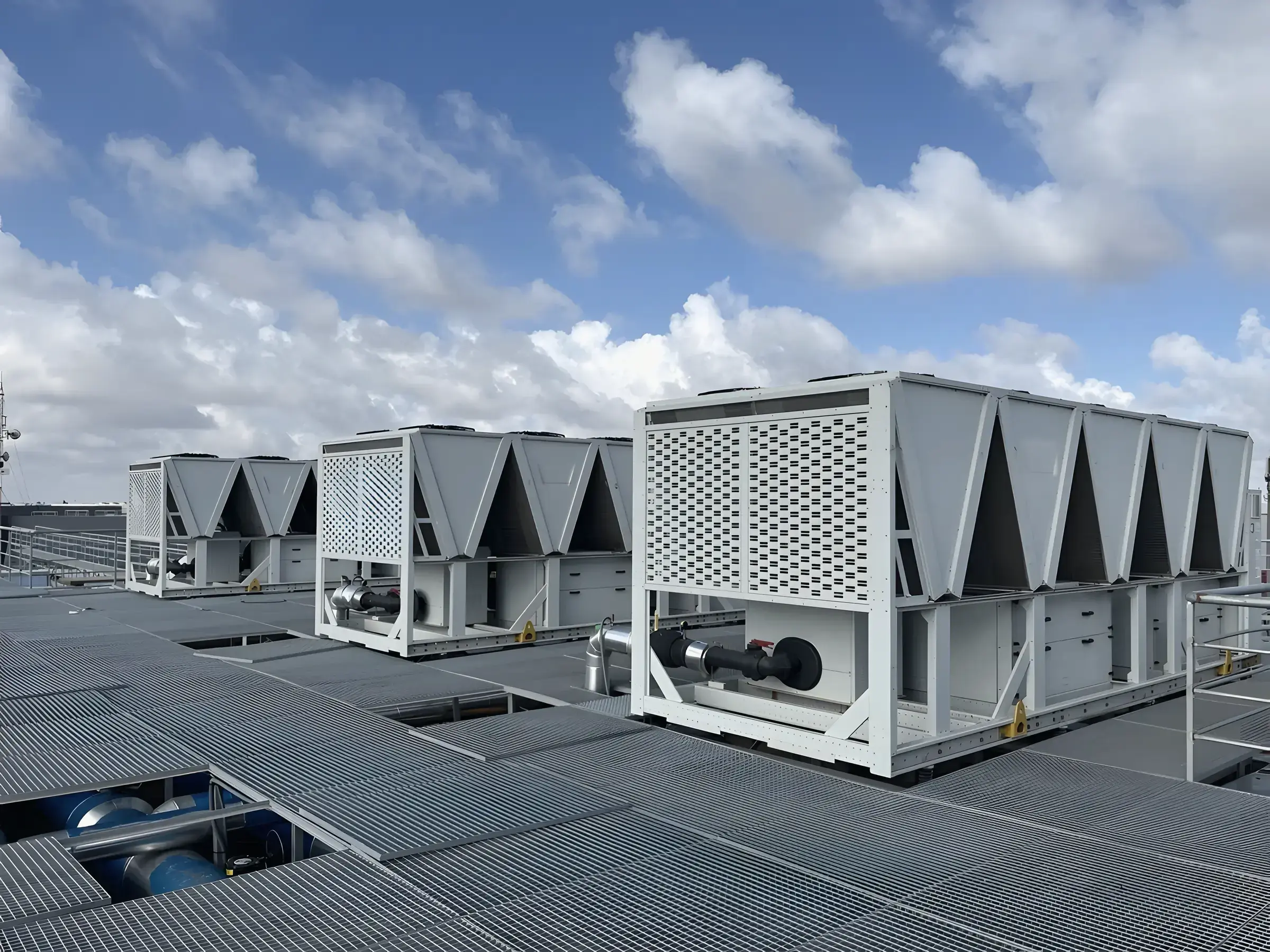A row of air-cooled chillers on a steel grating deck on the roof of the data center, under a cloudy sky
