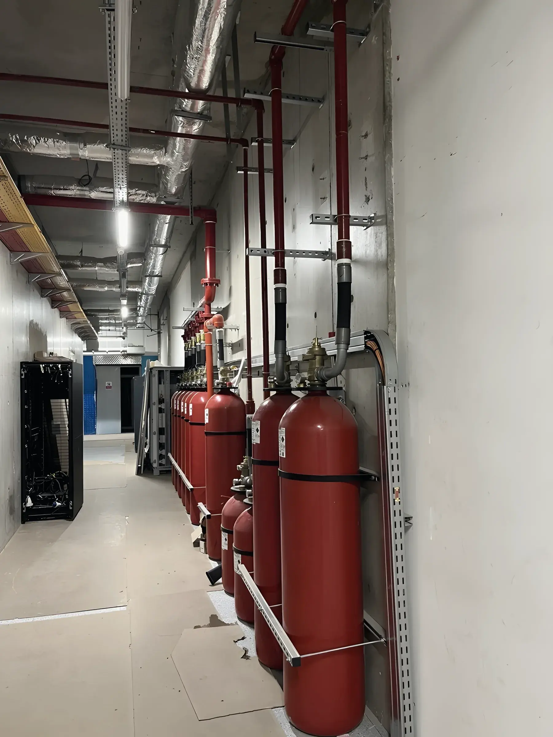 Clean-agent fire suppression cylinders and red pipework in a plant corridor