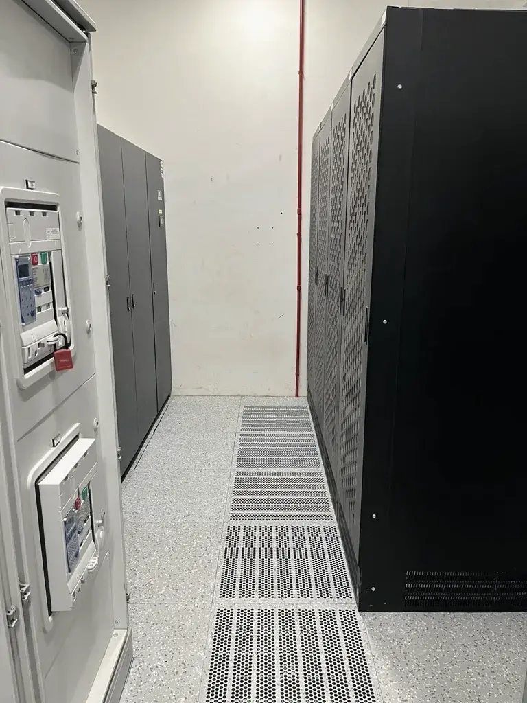 A UPS cabinet and a low-voltage switchboard either side of a grated corridor in an electrical room